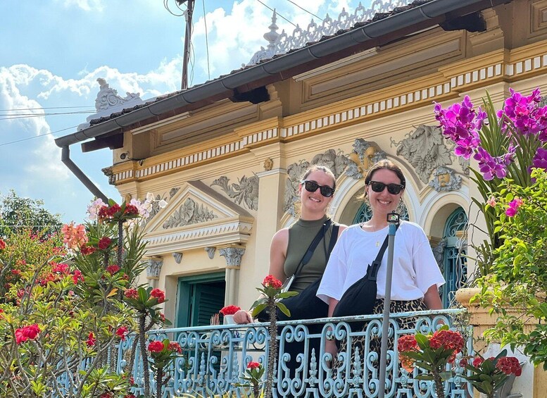 Two people on a balcony with ornate architecture and vibrant flowers. 4