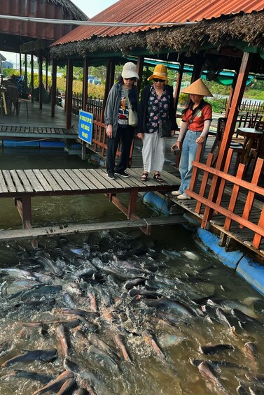A wooden bridge over a fish-filled pond with people standing on it. 5