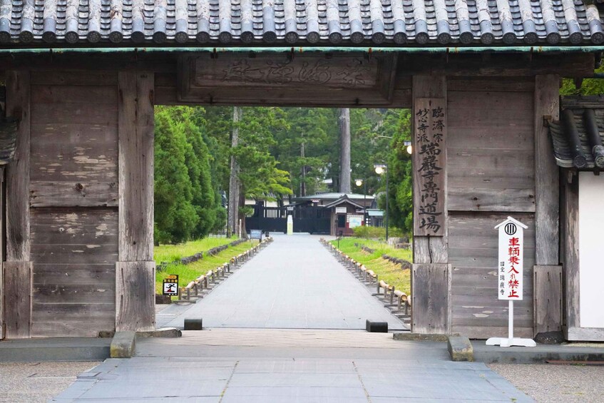 A traditional Japanese gate with wooden pillars and a tiled roof, leading to a pathway flanked by greenery. 3