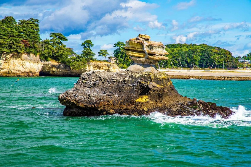 A rock formation in the ocean with a clear sky and greenery in the background. 4