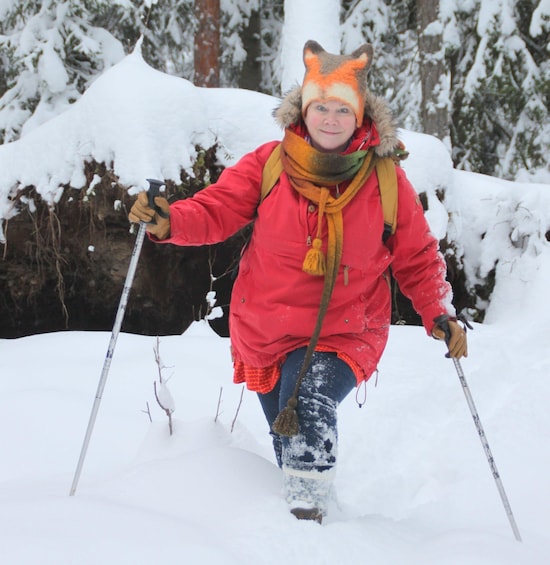 A person in a red coat and fox hat walking in the snow with ski poles. 3