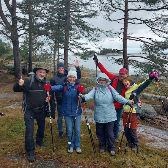 A group of people hiking with trekking poles, surrounded by trees and a body of water. 5