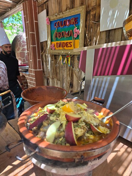 A food stall with a sign reading 'Colodge Aroma Pares' and a large clay pot filled with a dish of sliced apples and other ingredients. 4