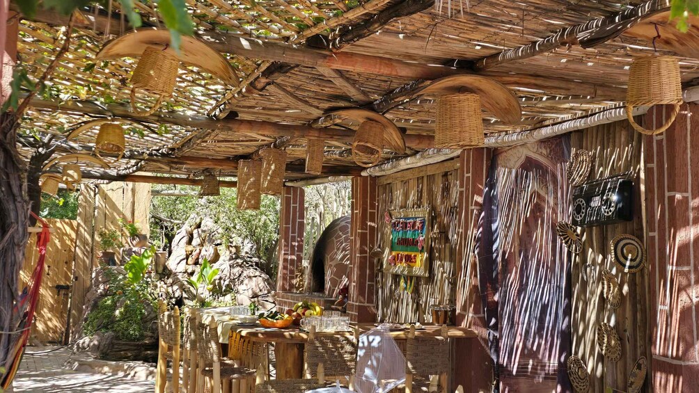 A rustic outdoor dining area with woven ceiling structures, wooden furniture, and decorative baskets. 3