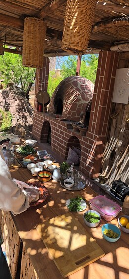 An outdoor cooking area with a brick oven, wooden cutting board, and various cooking utensils and ingredients. 5