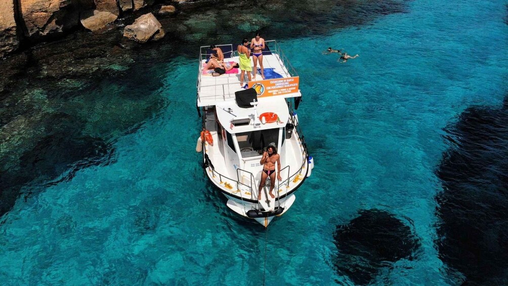 A boat with people on board, anchored in clear blue water with rocky shores nearby. 1