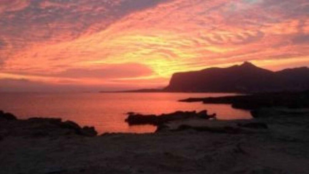 A sunset over a calm sea with a silhouette of a mountain in the distance. 3