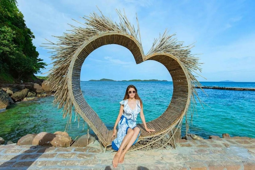 A person sitting inside a heart-shaped structure made of natural materials by a clear blue sea. 5