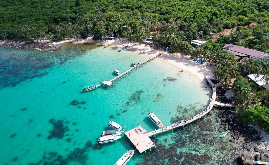 An aerial view of a tropical beach with clear turquoise waters, a pier, and boats docked. 1