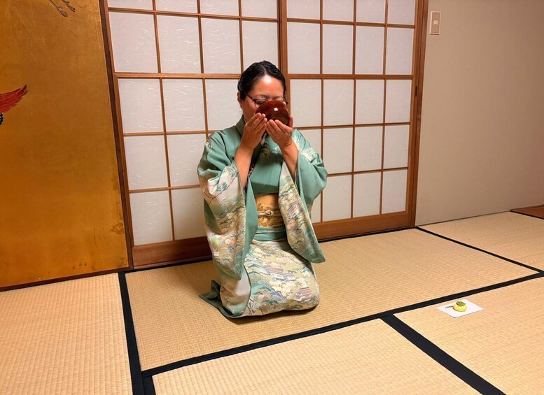 A person in traditional Japanese attire kneeling on tatami mat flooring. 2
