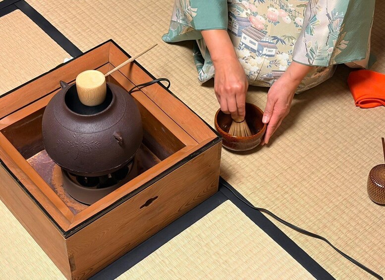 A person preparing matcha with a traditional Japanese tea bowl and a wooden matcha container. 4