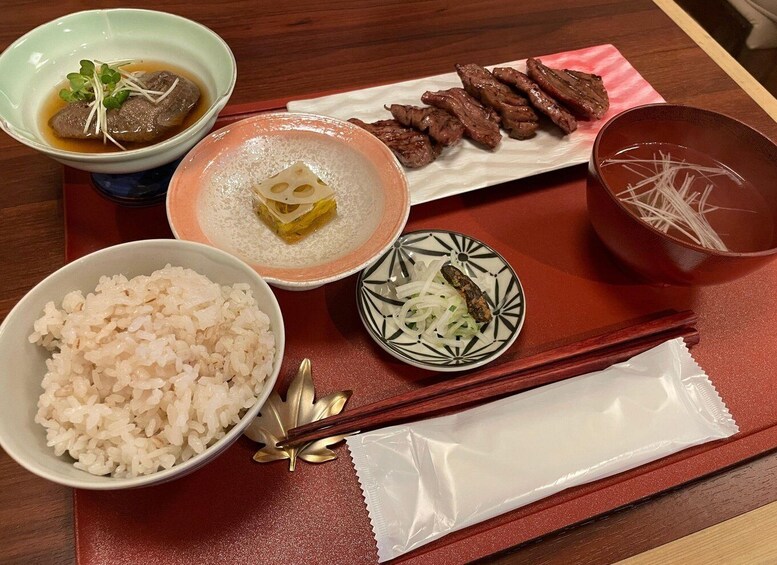 A traditional Japanese meal with rice, soup, beef, pickled vegetables, and noodles on a wooden tray. 3