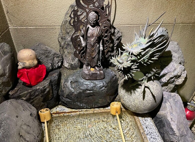 A rock garden with a statue, a small Buddha, and a vase with plants. 4