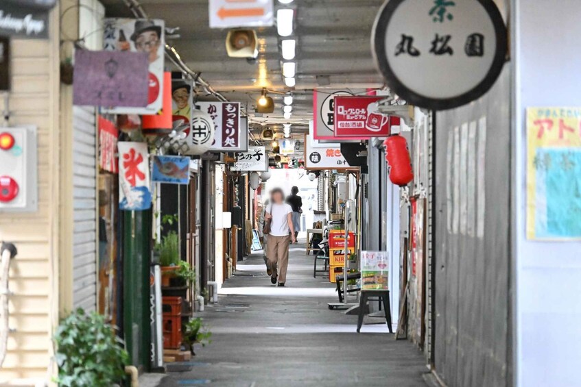 A narrow alley with various shops and signs, including a red lantern and a person walking down the path. 1