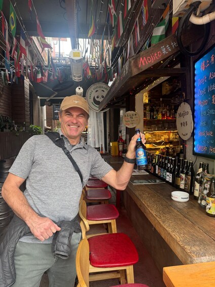 A bar with a wooden counter, red stools, and a variety of bottles. Flags are hanging from the ceiling, and a sign reads 'Mojo.' 3