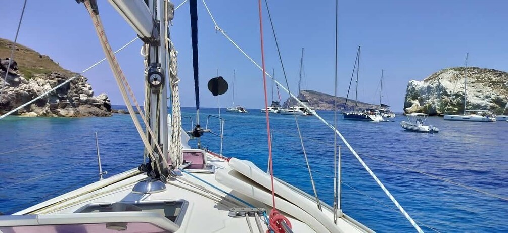 A sailboat with multiple masts and rigging, anchored near rocky coastlines with other boats in the background. 4