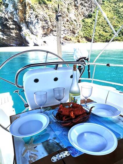 A table set with plates, glasses, and a bottle on a boat with a rocky coastline in the background. 5