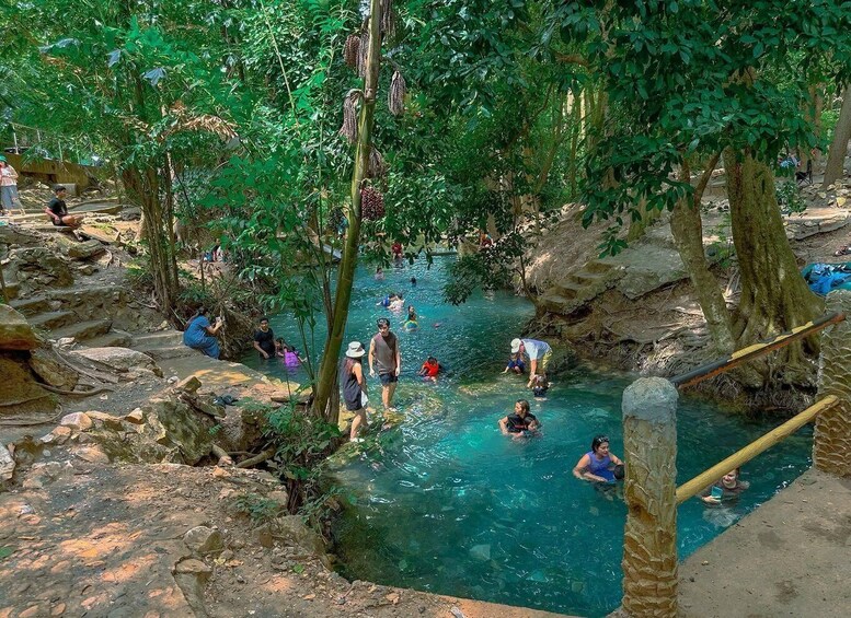 A natural pool surrounded by trees and rocks, with people swimming and relaxing. 2