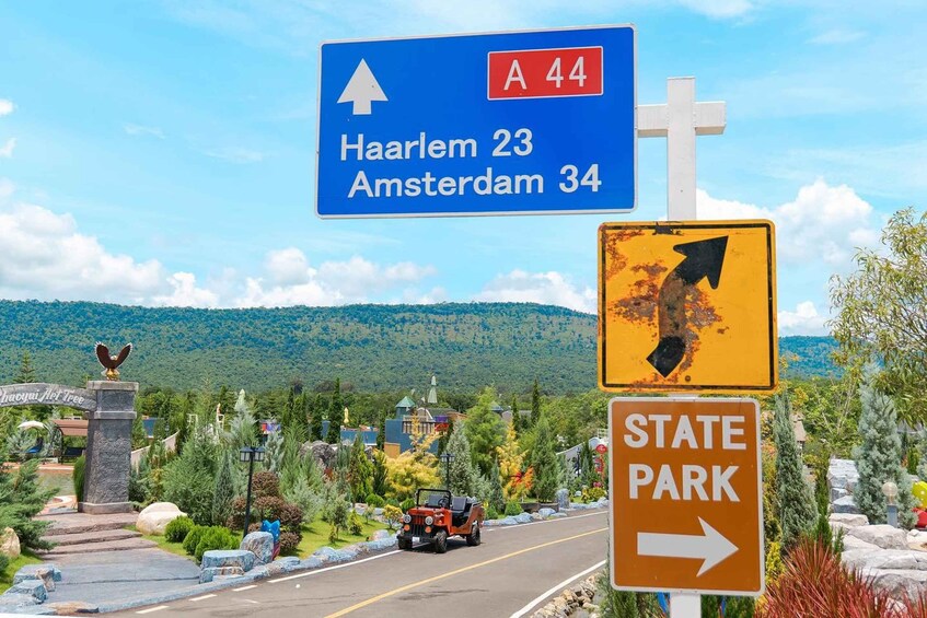A road sign for A 44 with directions to Haarlem and Amsterdam, a state park sign, and a Jeep on a road with a mountainous backdrop. 4