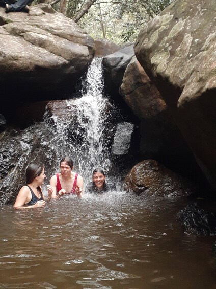 A waterfall in a rocky terrain with three people enjoying the water. 5
