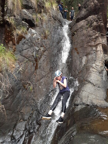 A person in a helmet and protective gear sliding down a rocky waterfall. 1