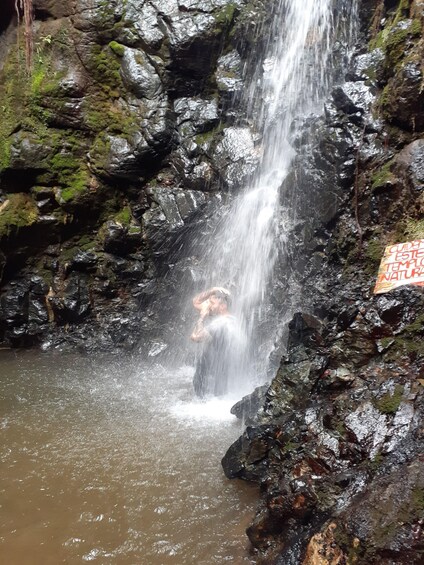 A waterfall in a rocky area with moss-covered stones and a person standing in the water. 3