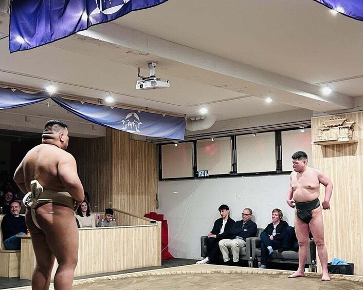 A sumo wrestling match in a room with spectators. 2