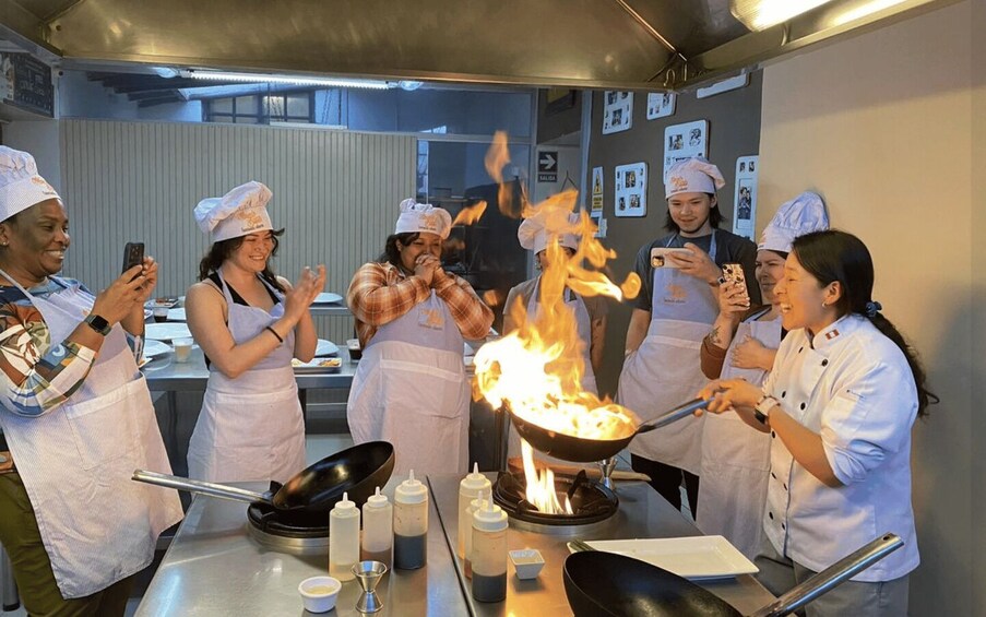 A group of chefs in a kitchen with a large wok on fire. 3