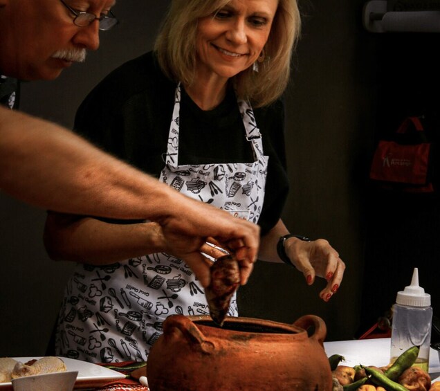A person cooking with a clay pot, vegetables, and a bottle of oil on the table. 2
