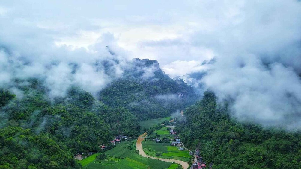A valley with a river, surrounded by dense forest and mountains, with a small settlement at the river's edge. 2