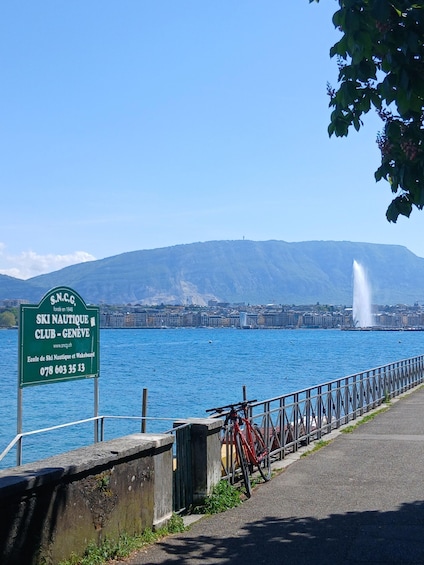 A sign for the Ski Nautique Club in Geneva, a bicycle, a fountain, and a mountain in the background. 2