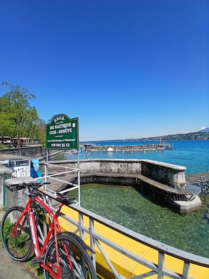 A clear blue sky, a sign for the Ski Nautique Club in Geneva, a red bicycle, and a yellow boat docked by the water. 4