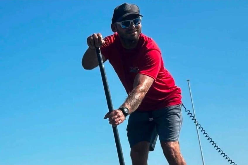 A person in a red shirt and cap holding a pole, standing on a dock. 5