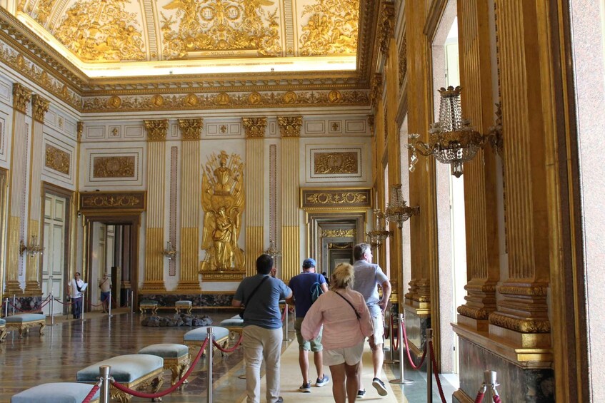 A grand hall with ornate golden decorations, a large statue, and a chandelier. 5