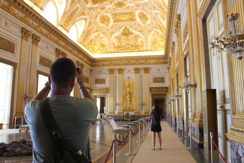 A man taking a photo inside a grand hall with ornate golden ceilings and columns. 4