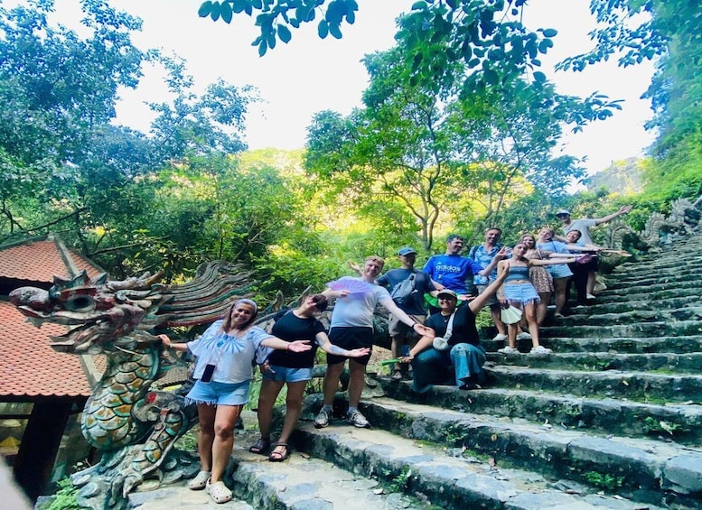 A group of people on stone steps surrounded by lush greenery and a traditional building with a tiled roof. 2