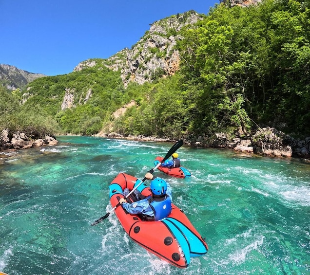 Two people kayaking on a clear turquoise river surrounded by green hills. 2