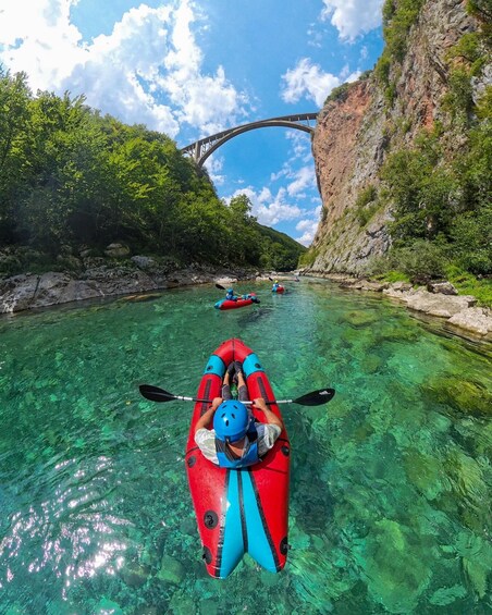 A clear river with kayaks, a rocky cliff, and a bridge in the background. 5