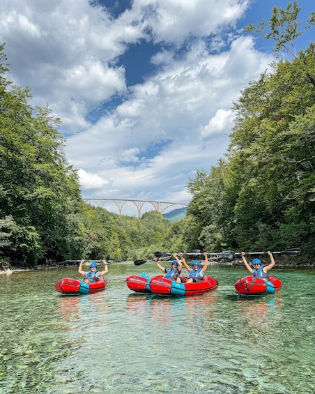 Three people in red inflatable rafts on a river with a bridge in the background. 1