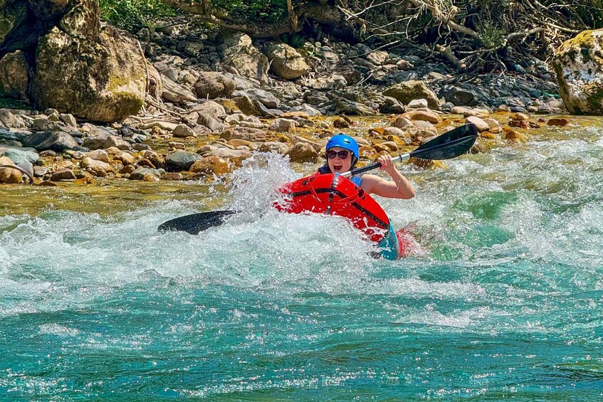 A person kayaking in a river with rocks and greenery in the background. 3
