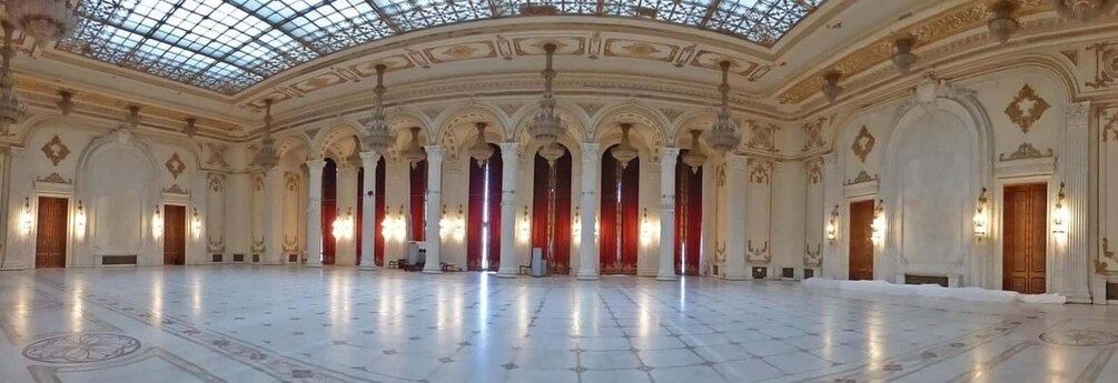 A grand hall with a high ceiling, ornate columns, and a patterned floor. 3