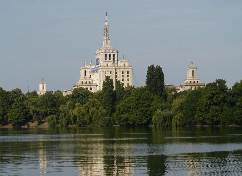 A large, historic building with a central tower and two smaller towers, surrounded by lush greenery and a calm body of water. 4