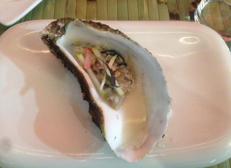 An oyster on a white plate with a salad inside. 2