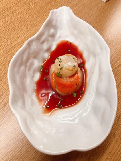A white ceramic dish with a scallop and sauce on a wooden table. 4