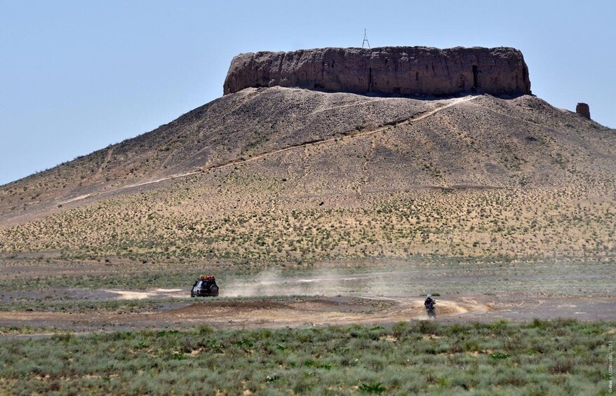 A large hill with sparse vegetation, a dirt road, and a vehicle in motion. 5