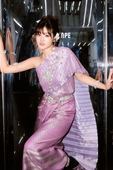 A person in a purple traditional outfit with intricate patterns, standing in front of a reflective glass surface. 5