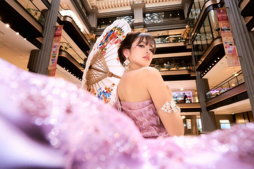 A person in a shopping mall with a decorative umbrella, surrounded by a blurred pink bokeh effect. 1