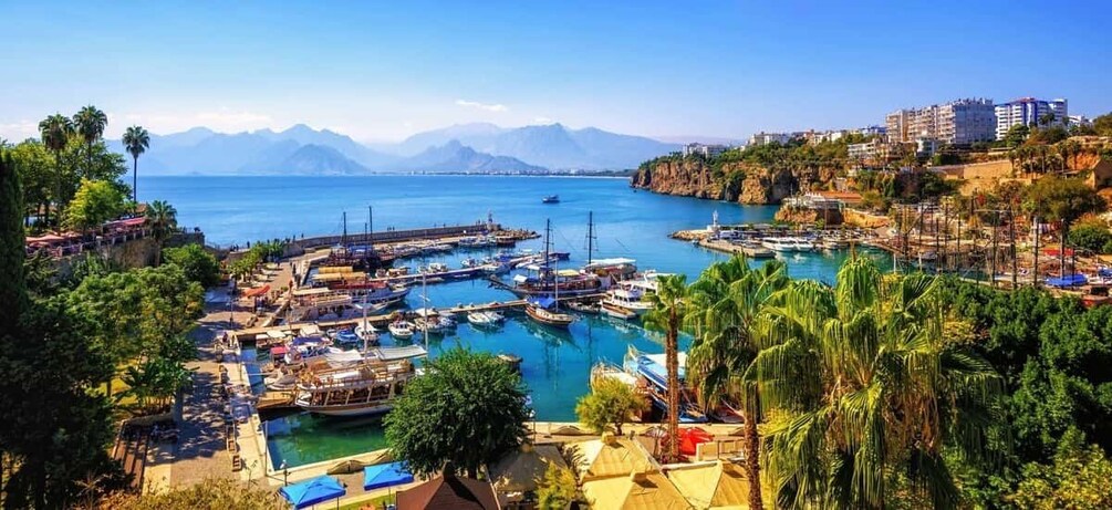 A coastal marina with boats, a clear blue sea, and mountains in the background. 4