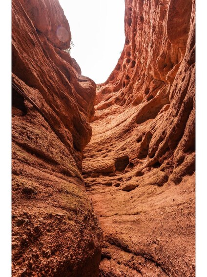 A narrow canyon with reddish rock formations and a visible hole in the wall. 5