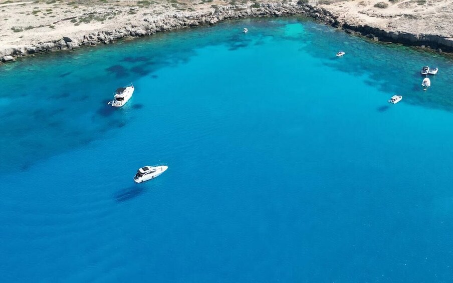 A clear blue sea with boats anchored near a rocky shoreline. 5